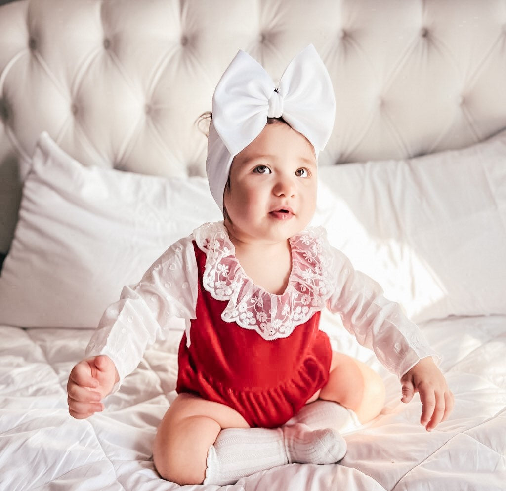 child wearing the Baby Girl Vintage Lace Red Velvet - White Sleeves Romper. Also has white boy headband on head, and white knee high socks.