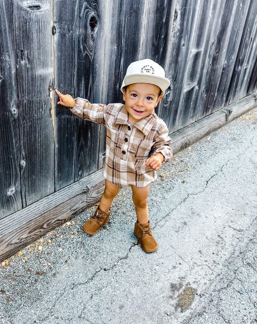 Kid wearing the Kids Dark Tan Plaid Hooded Flannel Romper with white hat & brown boots