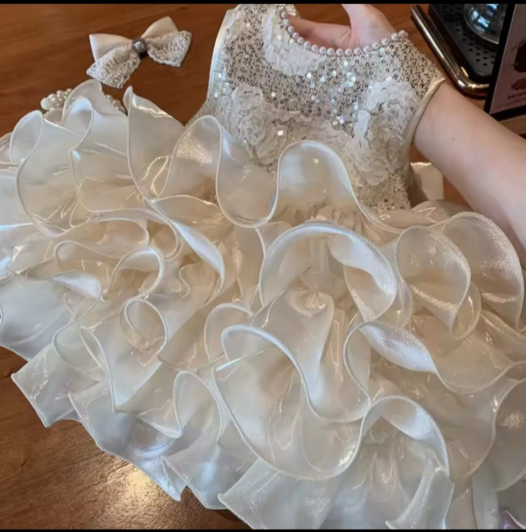 Close-up of a child's white dress with ruffles and a bow on a wooden surface