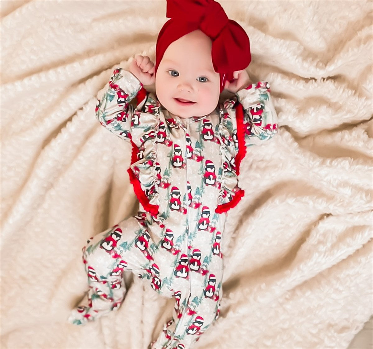 Kryssi Kouture Sienna Holiday Infant Deluxe Tutu Jumpsuit - Grey Penguin Pom. Child Wearing the ruffle shoulder jumpsuit with a red head wrap.