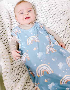 baby wearing sleeveless sleep bag with rainbow pattern on blue background