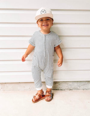 child wearing the Theo & Me Black & White Stripe Snaps - Side Pocket Romper, sandles & a white hat.