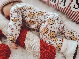 Sleeping kid wearing the Holiday Zippies Sleepers - Milk & Cookies with red check knit hat & white soft shoes