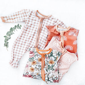 flat lay of Premier Baby Printed Bamboo Ruffle Zippies - Floral Melody + Rust Check + Rust with White Rainbows