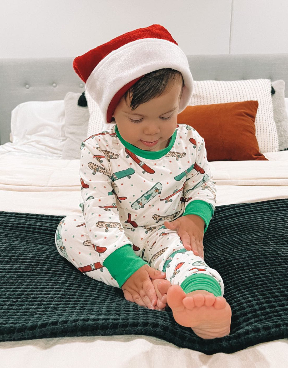 Kid wearing a 2 Pc Green Skateboard Pajama set, with a red santa hat