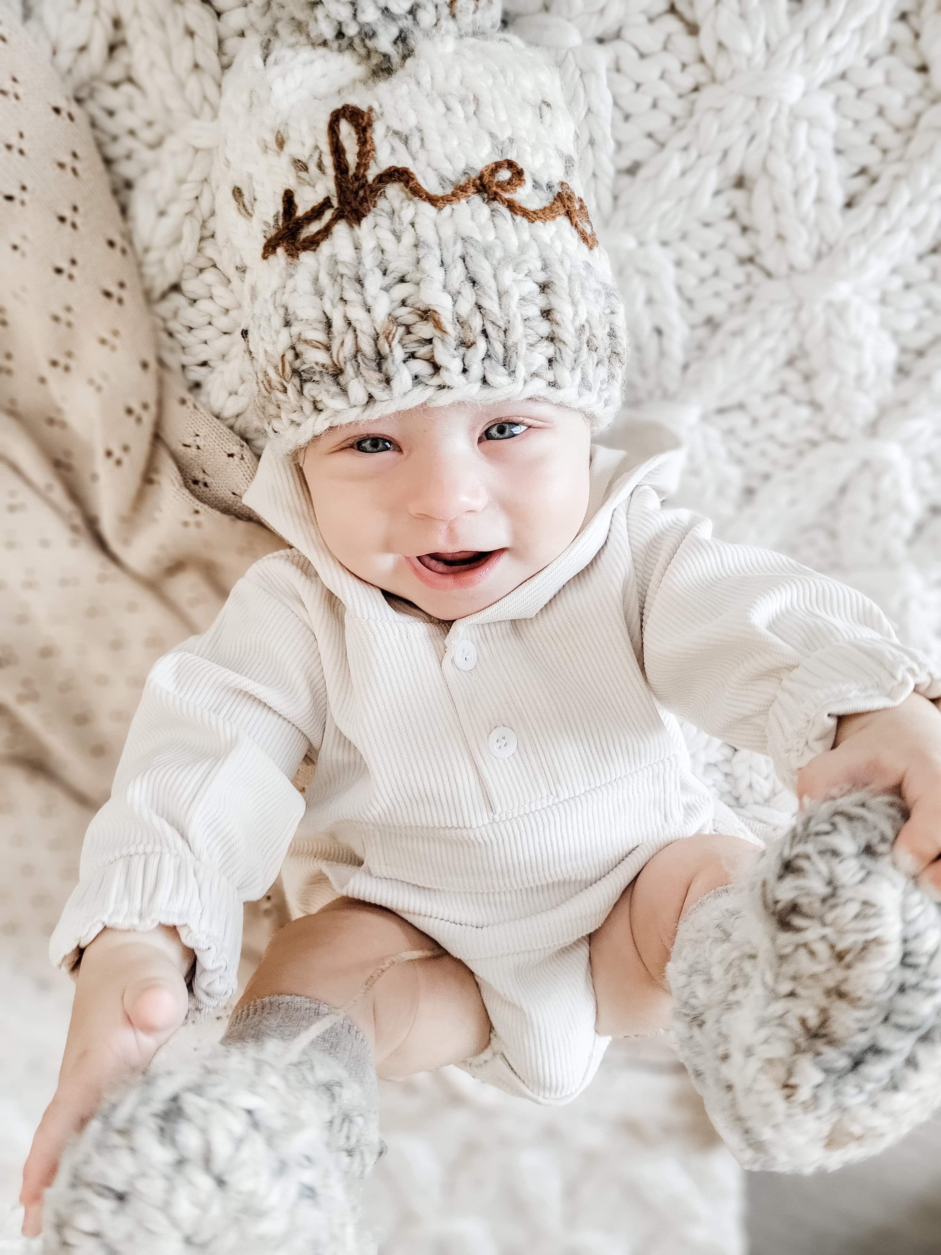 Baby wearing the Kids White Rib Hood Pocket Romper. 2 white buttons at chest, pocket with flap at stomach area, and rouged bits at the wrists. baby is also wearing a knit hat & socks.