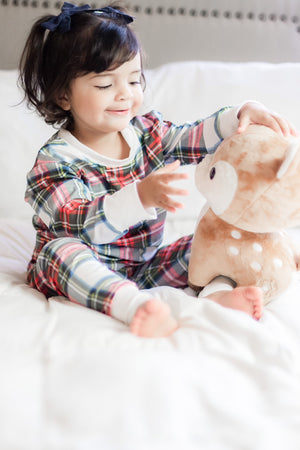 Young child wearing the 2 Pc Christmas Pajamas - Stuart Tartan Holiday Plaid, while playing with a reindeer stuffy.